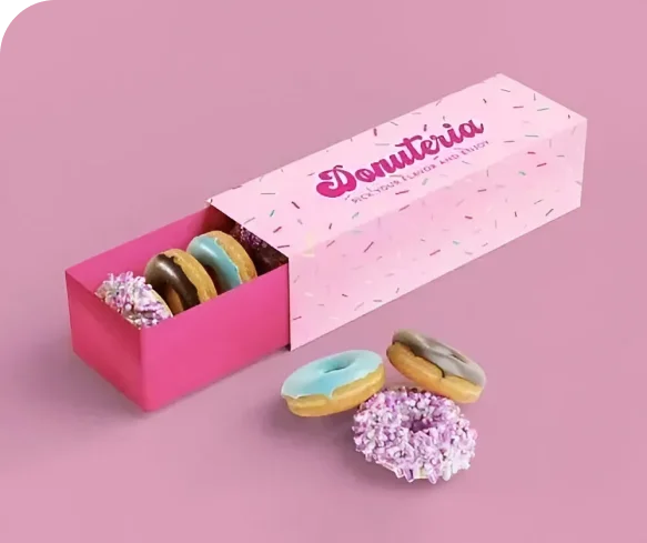 Pink Donutería sleeve & tray box with sprinkle pattern lid, bold white logo and tagline “Delicious donuts and more” printed on top. Inside: assorted decorated donuts.```